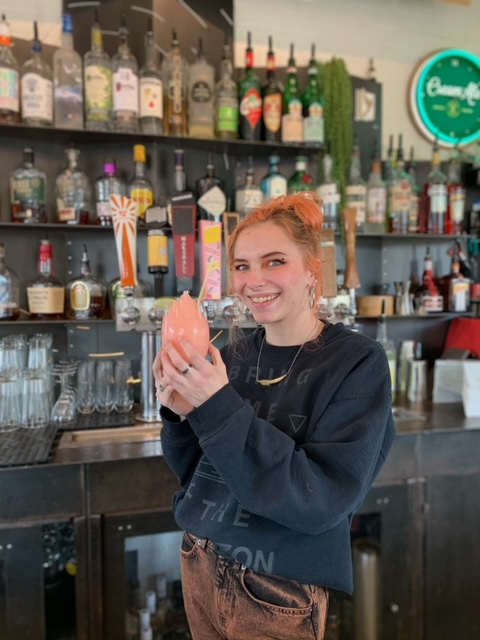a woman standing in front of a bar holding a drink
